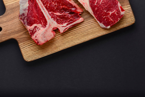 Fresh raw beef steak on wooden cutting board, top view. Served over black background. - Foto, Imagem