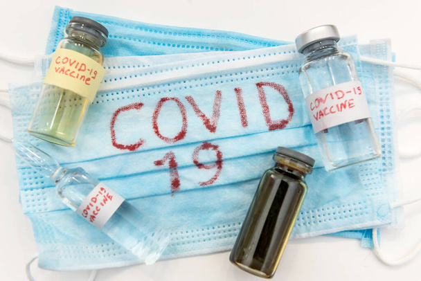 Coronavirus als gefährliche Krankheit. COVID-19 steht auf blauer medizinischer Gesichtsmaske und Virusimpfampulle. Epidemie - Foto, Bild
