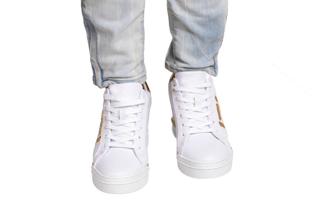 Women legs in jeans and sneakers. Woman legs in light denim pants wearing modern white sneaker. Fashionable white footwear. Macro photograph. - Photo, Image