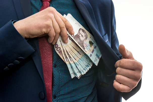 businessman takes a pack of Ukrainian money as a bribe and hides in his pocket in a jacket. Corruption and a trick. UAH. 1000 new banknote - Foto, imagen