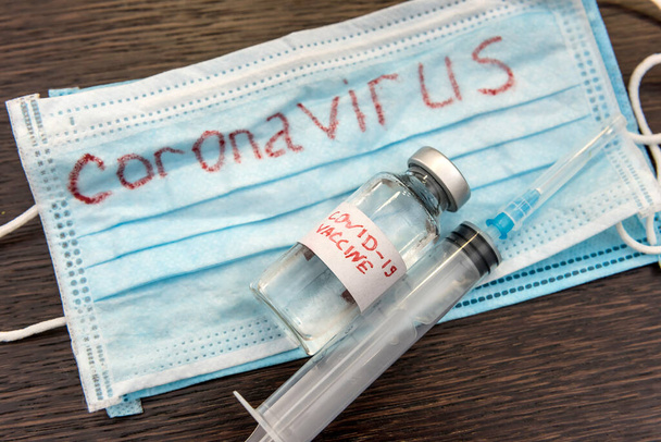 concept d'épidémie de coronavirus. masque médical avec une inscription rouge COVID-19 et une seringue avec un possible vaccin trouvé. pandémie. - Photo, image