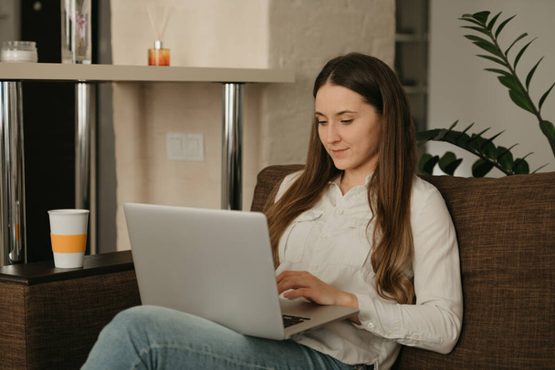 Praca zdalna. Biała młoda kobieta pracująca zdalnie na laptopie. Bizneswoman pracująca z domu na kanapie. - Zdjęcie, obraz