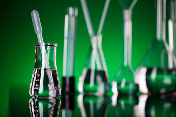 Coronavirus pandemic theme. Science research concerning fast covid tests and anti-covid vaccine. Beakers and test tubes on green background in laboratory. - Photo, Image