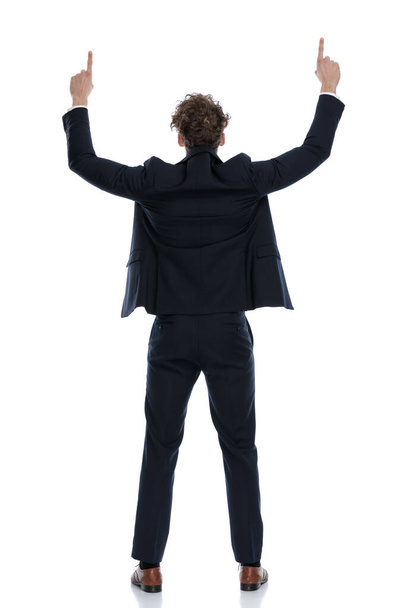 Бізнесмен, який вказує обидві руки, одягнений у костюм і стоїть на білому фоні студії
 - Фото, зображення