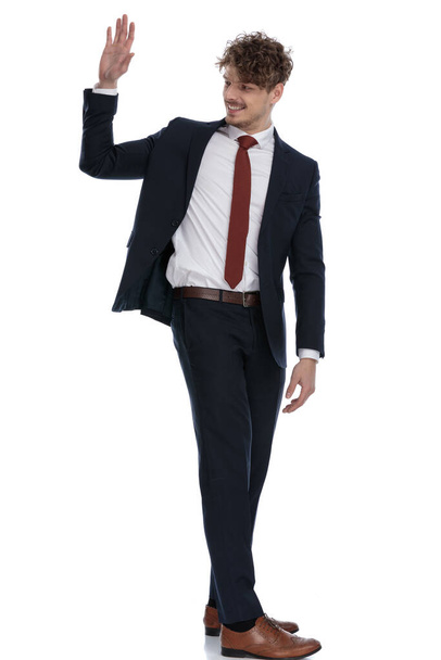 Вид збоку щасливого бізнесмена, який посміхається і махає в костюмі і стоїть на білому фоні студії
 - Фото, зображення