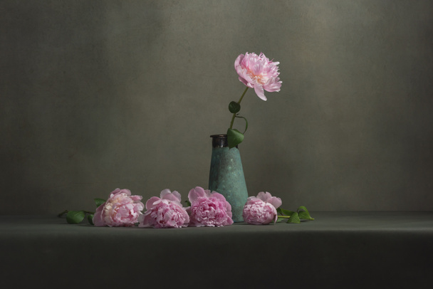 Vintage pottery vase with one peony and some peonies lying next to it on a table in a grey room. - Photo, Image