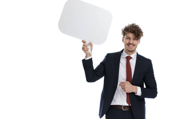 Happy businessman holding speech bubble and laughing while wearing suit and standing on white studio background - Photo, Image
