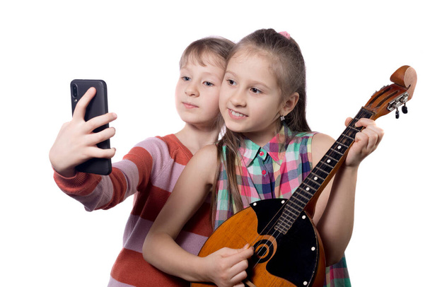 Two cute little girls take selfie on a smartphone. Studio photo on a white background. - 写真・画像