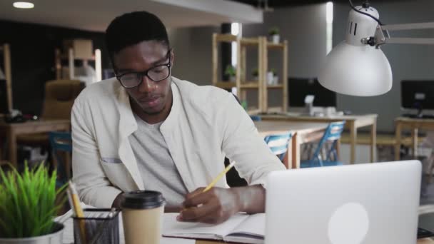 Συγκεντρωμένος νεαρός Αφρικανός που γράφει και εργάζεται σε φορητό υπολογιστή στο γραφείο - Πλάνα, βίντεο