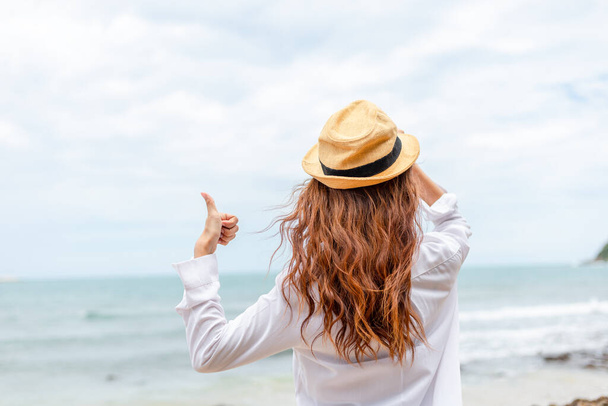 smiling young woman in sun hat and finger thumb up on beach. summer, holidays, vacation, travel concept - Photo, image
