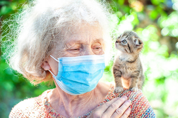 Милая пожилая женщина в саду держит шотландского котенка на плече. Карантин, изоляция. Коронавирус ковид-19. Домашние животные помогают пожилым людям справиться с одиночеством. Одиночество. Уход за животными
 - Фото, изображение