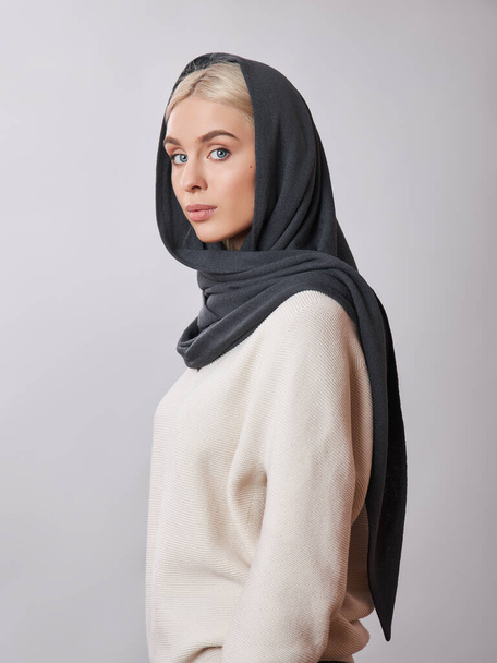European Muslim woman with a blonde hair in a headscarf shawl dressed on her head. Beautiful girl in sweater with soft skin, natural cosmetics - Foto, afbeelding