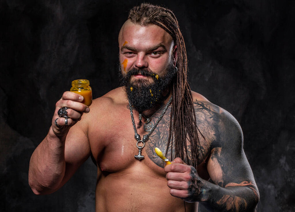 athletic man with beard and tattoos eats baby food, leads a healthy lifestyle - Photo, Image