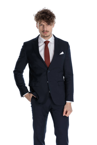Bothered businessman frowning with hand in pocket while wearing suit and standing on white studio background - Foto, imagen