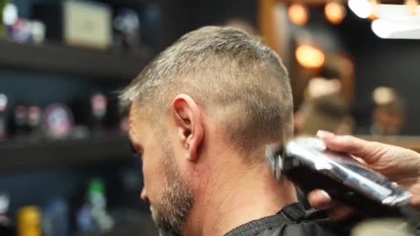 Barber woman cuts bearded mans hair with a clipper in barbershop. Mens hairstyling and hair cutting in salon. Grooming the hair with trimmer. Hairdresser doing haircut in retro hair salon. - Video, Çekim