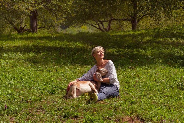 femme au repos avec un enfant sur l'herbe ; fille caressant une chèvre. amitié des personnes et des animaux dans une ferme
. - Photo, image