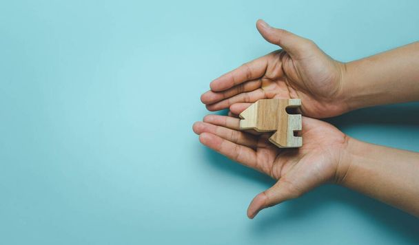 Luftbild von der Tischplatte, wie Hände ein Haus aus Holz auf blauem Papier mit Kopierraum halten. Sicher zu Hause bleiben zur sozialen Distanzierung von Coronavirus (Covid-19) oder obdachlosem Leihkonzept. Familie international - Foto, Bild