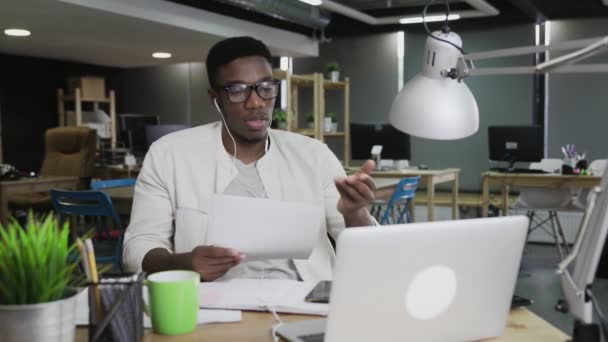 Homem africano com fones de ouvido tem uma conversa em vídeo conferência no escritório moderno
 - Filmagem, Vídeo