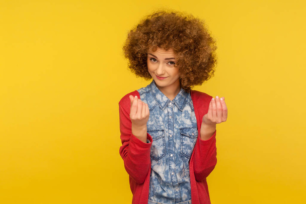 Give me cash! Portrait of enterprising woman with curly hair showing money gesture, hinting at salary increase, having business idea to earn income. indoor studio shot isolated on yellow background - Foto, imagen