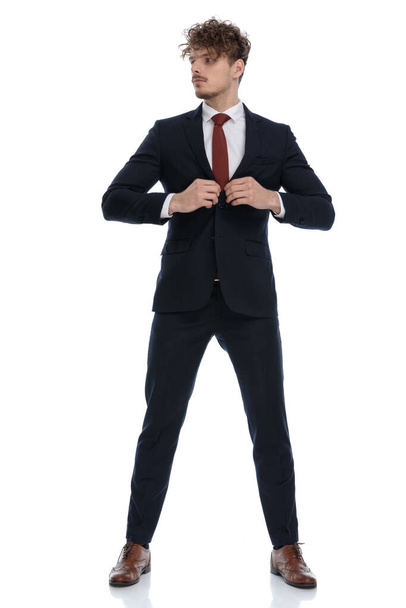Determined businessman looking away and adjusting his jacket while wearing suit and standing on white studio background - Фото, зображення