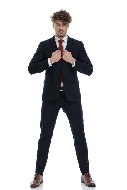 Empresário confiante ajustando seu colarinho enquanto vestindo terno e de pé no fundo do estúdio branco
 - Foto, Imagem