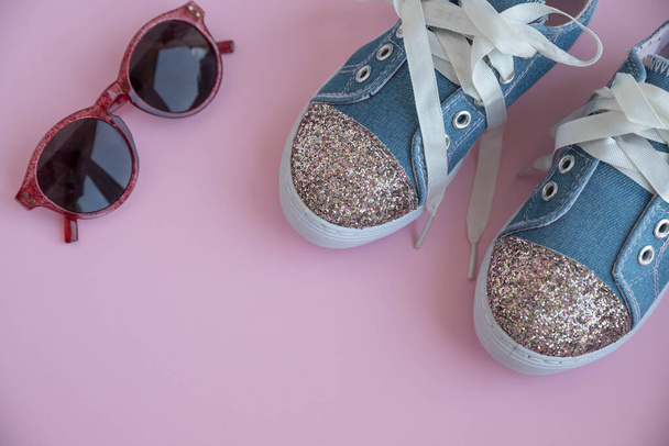 Дитячі текстильні мереживні кросівки. взуття для дівчаток на рожевому тлі. Модне дитяче взуття. Розумне повсякденне модне джинсове та блискуче взуття. Окуляри та модне дитяче спортивне взуття. Копіювання простору. Вибірковий фокус
 - Фото, зображення