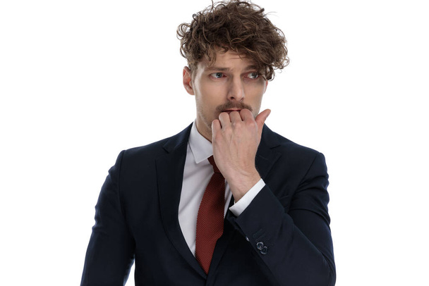 Afraid businessman looking away with hand on chin while wearing suit and standing on white studio background - Photo, Image