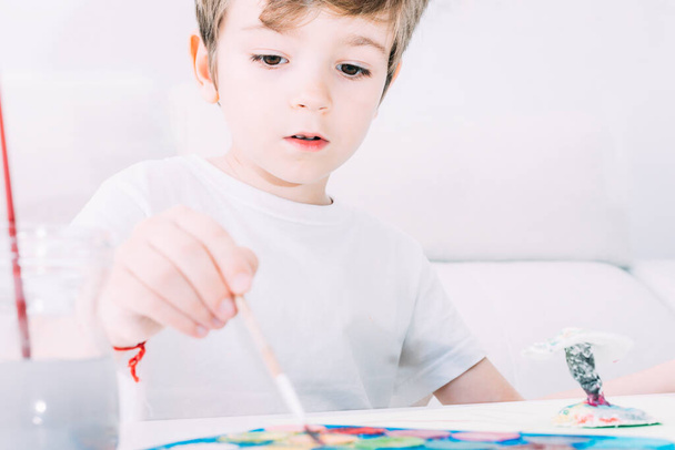 Προσεκτική παιδική ζωγραφική με πινέλο στο χέρι και χρωματιστές ακουαρέλες. - Φωτογραφία, εικόνα