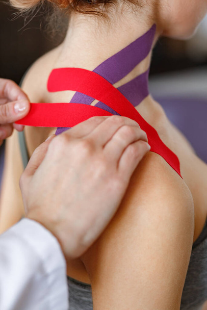 Kinesiology taping. Physical therapist applying kinesiology tape to patient neck. Therapist treating injured trapezius muscles of young athlete. Post traumatic rehabilitation, sport physical therapy - Φωτογραφία, εικόνα