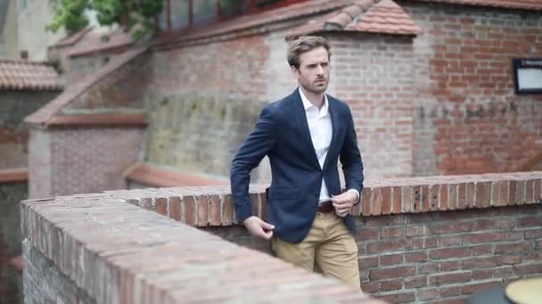 smart casual elegant businessman leaning on a brick wall, pulling out his hand from his pocket, crossing his arms to chest, and fixing his jacket - Footage, Video