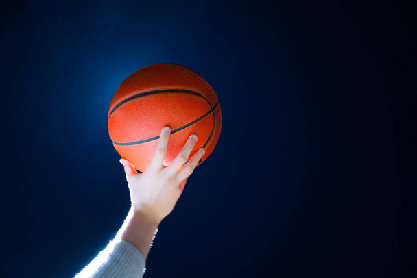 Κοντινό πλάνο του επαγγελματία μπασκετμπολίστα κρατώντας μια μπάλα στο χέρι. Street μπάσκετ αθλητής με μια μπάλα και μπλε ουρανό στο παρασκήνιο - Φωτογραφία, εικόνα