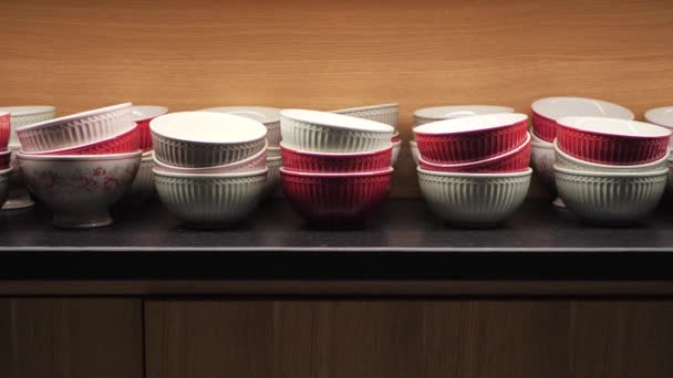 Rote und weiße Keramikschalen in einem hölzernen Küchenschrank. Geschirr von oben beleuchtet in einem Schrank mit modernem Interieur - Filmmaterial, Video