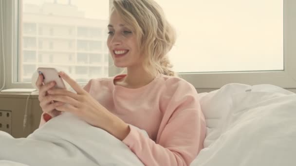 Happy cheerful blonde woman indoors at home using mobile phone - Video, Çekim