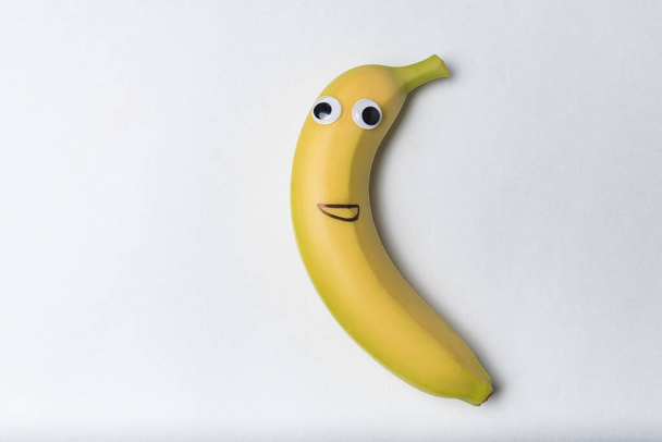 Bananowa postać z zabawną twarzą na białym tle. Banan z Google oczy i malowane uśmiech. - Zdjęcie, obraz