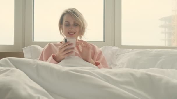 Positive blonde woman indoors at home using mobile phone - Felvétel, videó