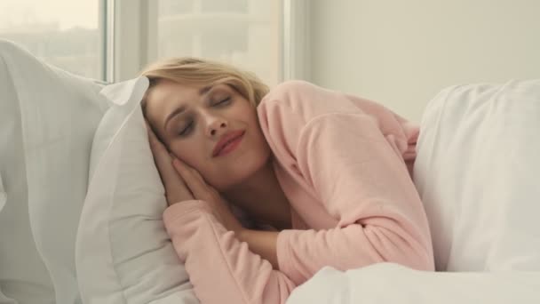 Pretty blonde woman awake indoors at home lies in bed - Materiał filmowy, wideo