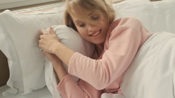 Pretty blonde positive woman indoors at home lies in bed - Imágenes, Vídeo