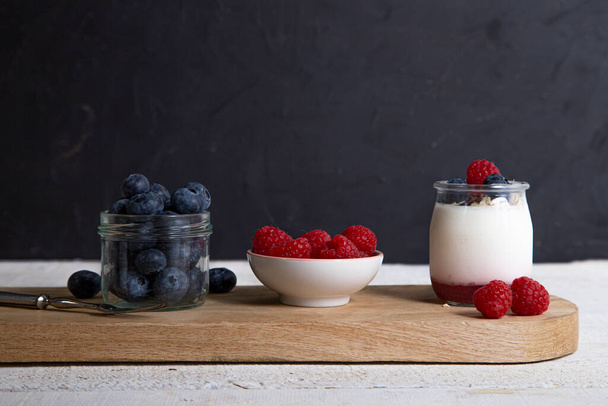 Petit déjeuner avec yaourt blanc aux framboises fraîches, bleuets et muesli sur table de service sur table rustique. Concept de vie saine
. - Photo, image