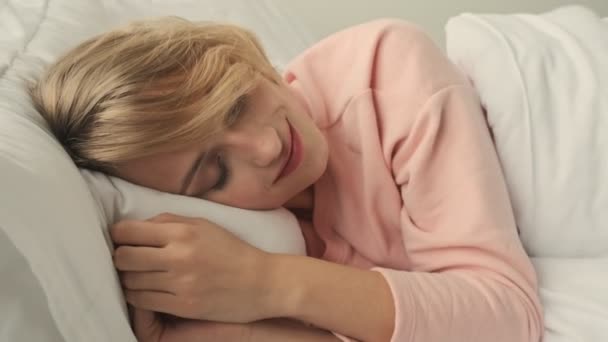 Smiling blonde positive woman indoors at home lies in bed - Záběry, video