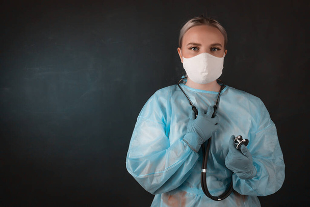 Portrait of a doctor in a mask and medical gown on a black background. Copy space - Foto, Bild