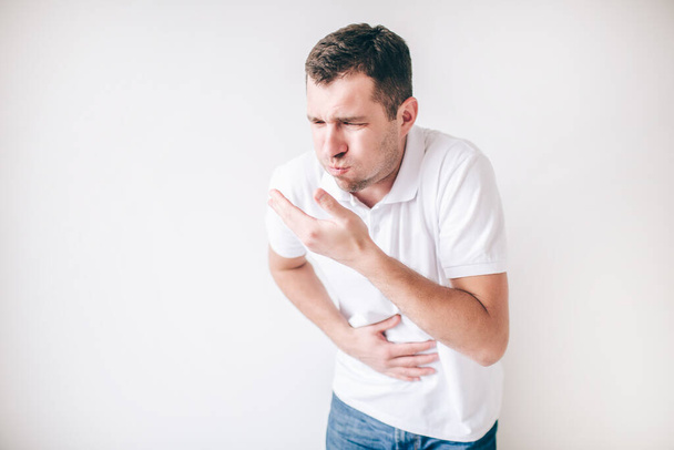 Young sick man isolated over white background. Almost vomiting into hand. Bad digestion and sickness. Guy suffer from pain and ache in stomach. - 写真・画像
