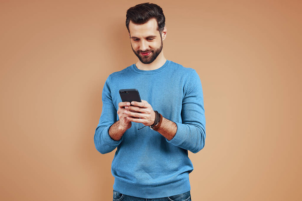 Lächelnder junger Mann in Freizeitkleidung mit digitalem Tablet vor braunem Hintergrund - Foto, Bild