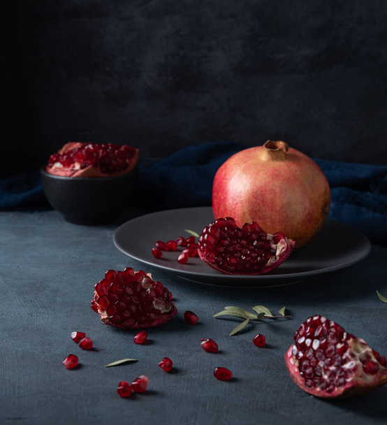 a juicy and fresh  pomegranate lies on gray  plate on a dark background. Dark and mood photo - Fotografie, Obrázek