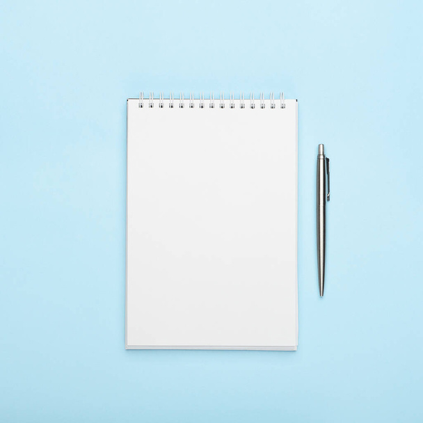 Белый блокнот с металлической ручкой на синем фоне. Office, copy space, mock up, template, top view, flat lay
 - Фото, изображение
