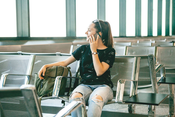 フライトを待っている間、空港で携帯電話や携帯電話で話している女の子の観光客や学生. - 写真・画像