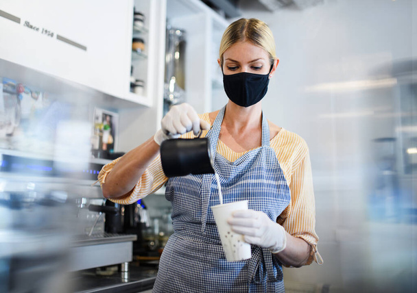 Coffee shop woman owner working with face mask, open after lockdown quarantine. - 写真・画像