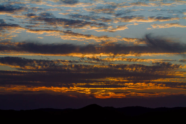 Atardecer entre nubes oscuras en un cielo naranja y azul - Fotoğraf, Görsel