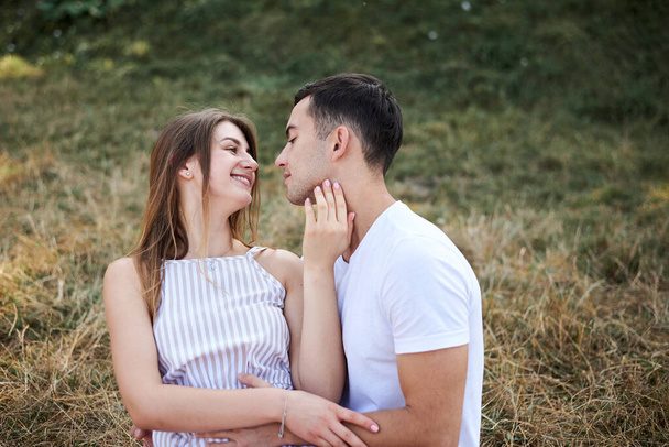 Молода пара закохалася, сидячи на зелено-жовтому газоні, обіймаючи поцілунки. Блондинка одягнена в стриптиз-короткометражний і брюнетка чоловік у білих футболкових синіх шортах на романтичному побаченні. Відносини
 - Фото, зображення