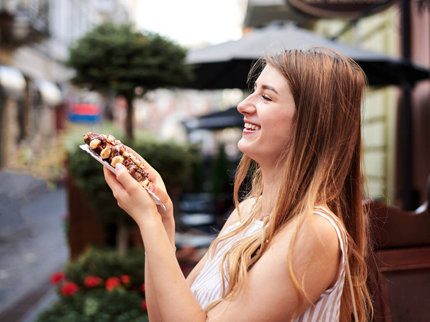 Romantic couple on date eating tasty belgian waffle with chocolate and caramel. Young blond woman, feeding brunette man with yummy desert in summer in the morning. Nutritious breakfast, snack. - Photo, image