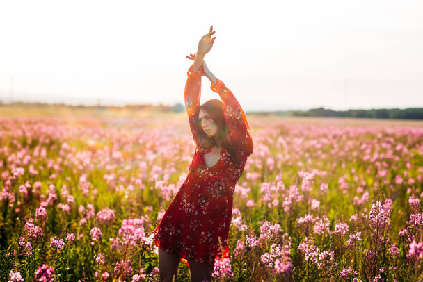 Mooi, lang, jong meisje, lang haar, rode jurk in een veld met rode bloemen. - Foto, afbeelding